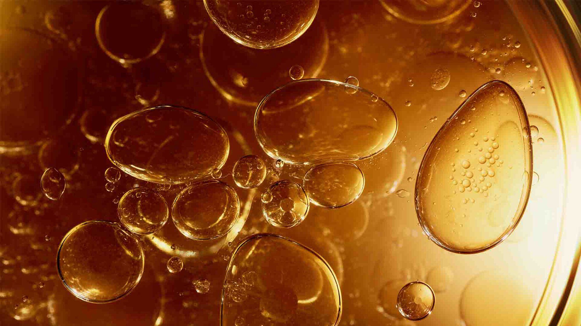 Blasen schweben in bernsteinfarbener Flussigkeit, zusatzlich beleuchtet fur ein glanzendes Aussehen.