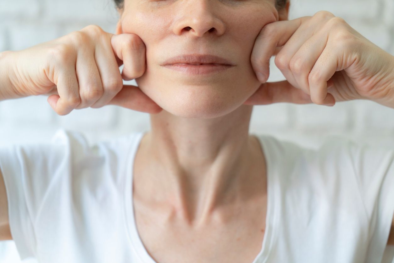 Frau in weißem T-Shirt zieht mit ihren Fingern ihre Wangen zuruck