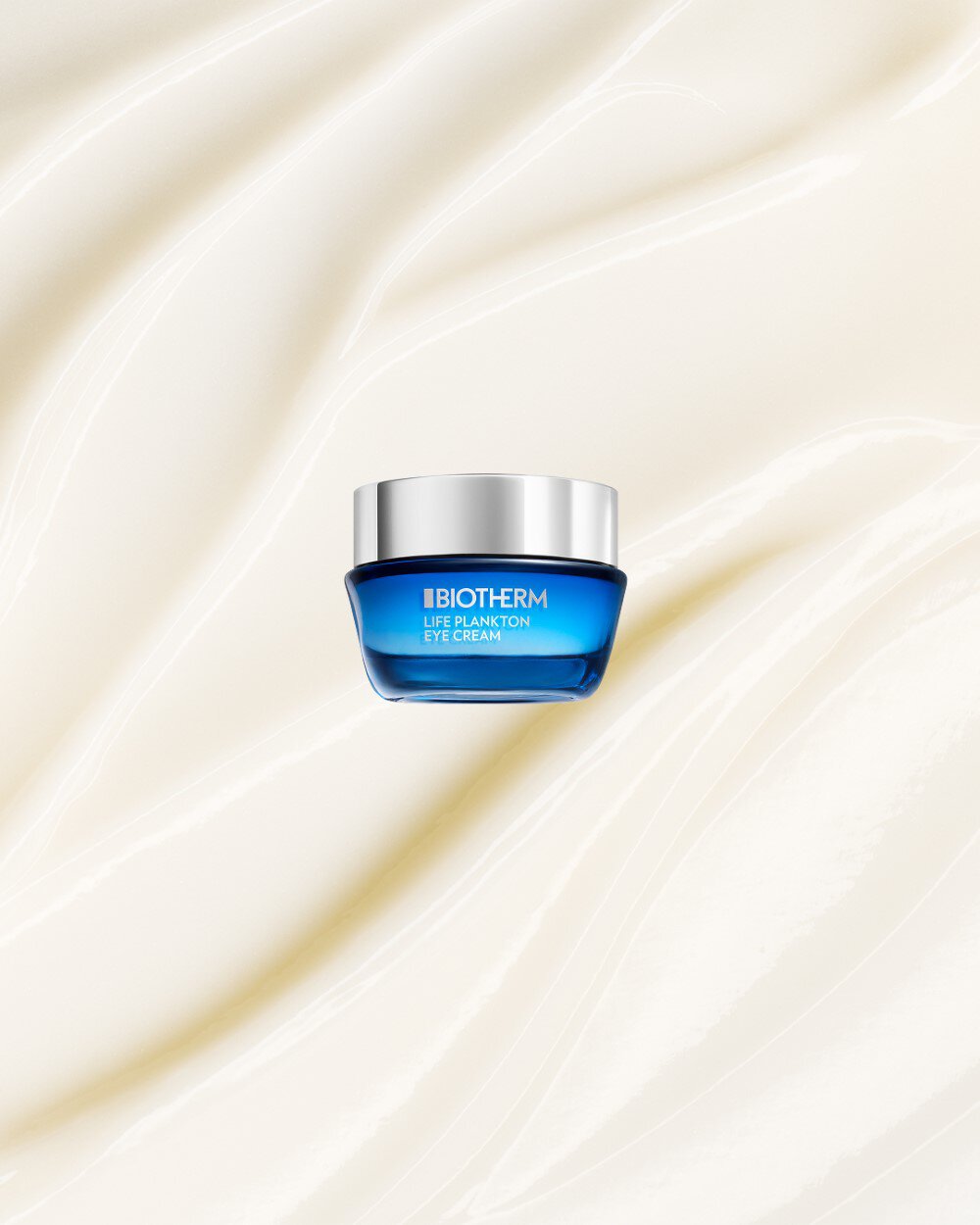 Cremeglas mit silbernem Deckel schwebt vor einem beigen, wellenformigen Hintergrund. Text: "BIOTHERM LIFE PLANKTON EYE CREAM".