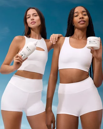 Zwei Frauen in weißen Sportoutfits mit BIOTHERM Pflegeprodukten vor blauem Himmel.