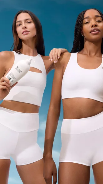 Zwei Frauen in weißen Sportoutfits mit BIOTHERM Pflegeprodukten vor blauem Himmel.