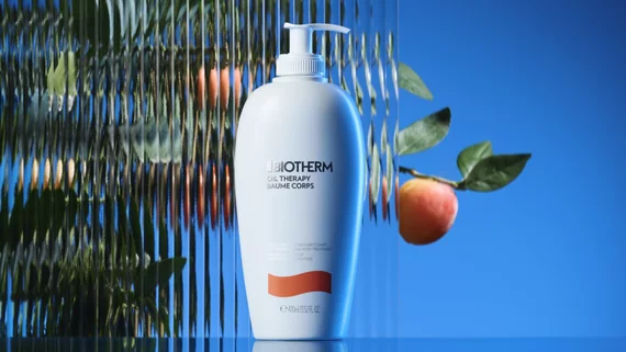 Pumpspender mit "BIOTHERM OIL THERAPY BAUME CORPS" vor blauem Hintergrund und Baum mit Fruchten.