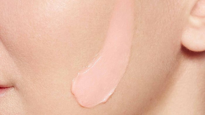 Rosa Creme wird auf eine Gesichtshaut aufgetragen, was eine Nahaufnahme des Hautpflegerituals zeigt.