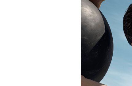 Ein Mann halt eine schwarze Kugel im Freien, Himmel im Hintergrund.