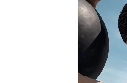 Ein Mann halt eine schwarze Kugel im Freien, Himmel im Hintergrund.