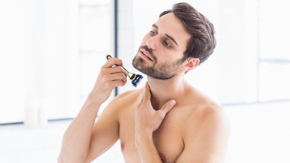 Ein Mann rasiert sich vorsichtig sein Gesicht in einem hell erleuchteten Badezimmer.