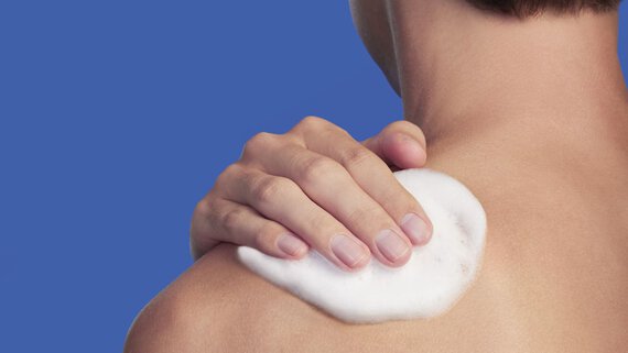 man applying shower gel on his shoulder