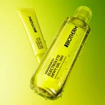 Transparente Flasche und gelbe Tube Biotherm Aquasource+ Eau de Lait Demaquillante mit sichtbaren Wassertropfen vor leuchtend grunem Hintergrund.