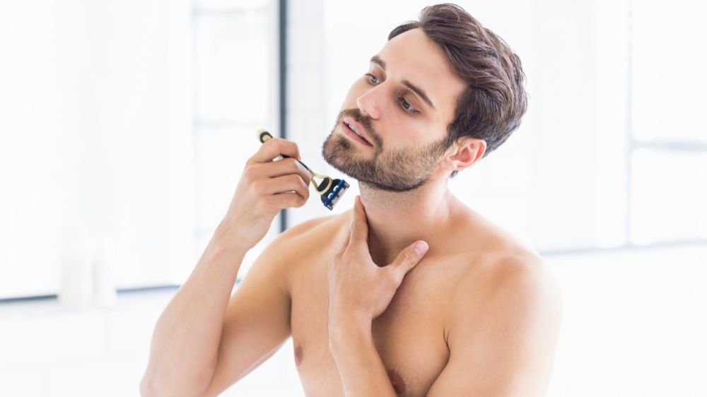Ein Mann rasiert sich das Gesicht in einem hellen Badezimmer.