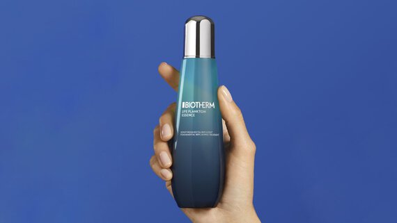 Hand halt eine Biotherm-Flasche vor blauem Hintergrund. Text: "BIOTHERM LIFE PLANKTON ESSENCE".
