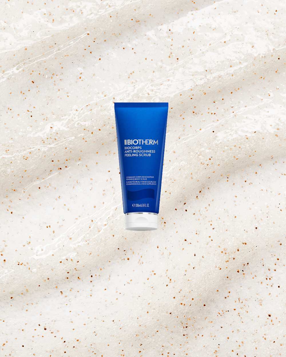 Blaue Tube, stehend auf heller Flache mit Kornchen, enthalt Text: "BIOTHERM BIOCORPS ANTI-ROUGHNESS PEELING SCRUB".