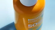 Orangene WATER LOVER SUN MILK SPF 50 Flasche mit weißem Deckel vor hellblauem Hintergrund.