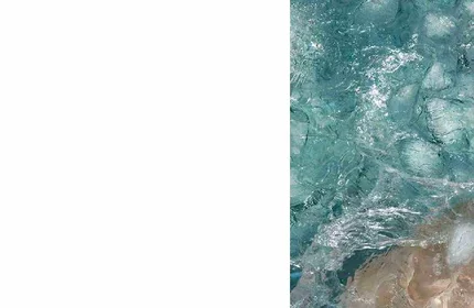 Turkisblaue Wellen brechen an einem sandigen Strand, umgeben von schaumendem Wasser.