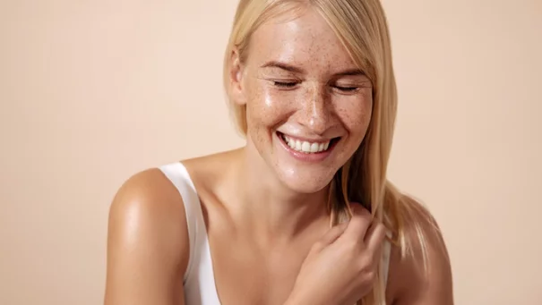 Woman is looking at the camera and holding her hand in front of her face to protect from the sun