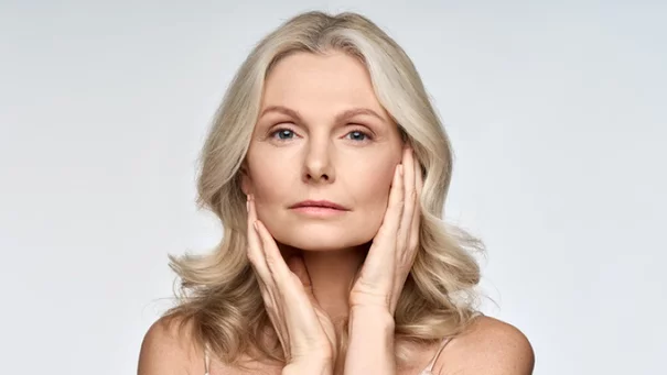 Frau mit blonden Haaren halt ihr Gesicht mit den Handen, neutraler Gesichtsausdruck, weißer Hintergrund.