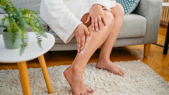 Person cremt Beine auf Sofa; Wohnzimmerumgebung mit Teppich und Tisch.