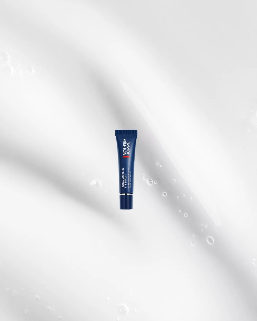 Eine dunkelblaue Tube auf weißem Hintergrund mit Wassertropfen. Text: "BIOTHERM HOMME FORCE SUPREME EYE ARCHITECT SERUM."