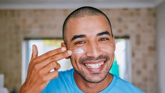 Lachelnder Mann mit Anti-Aging-Creme auf Wange