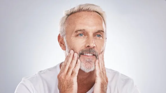 Un hombre de cabello y barba blancos se toca la cara.