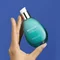 Hand halt eine turkisfarbene Biotherm-Flasche mit Spender vor blauem Hintergrund. Text: "BIOTHERM... REJETON IQ...".