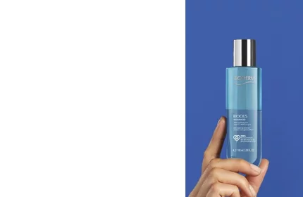 Hand halt blaue Flasche mit silbernem Deckel vor blauem Hintergrund, darauf steht: "BIOTHERM BIOCILS".