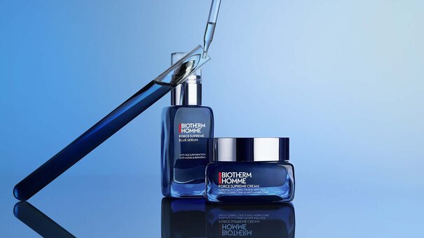 Zwei blaue Biotherm HOMME Produkte neben Pipette auf reflektierendem Untergrund, umgeben von blauem Licht.