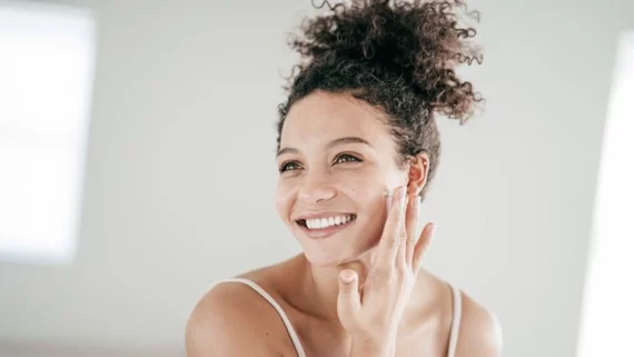Una mujer sonriente aplicando crema facial.