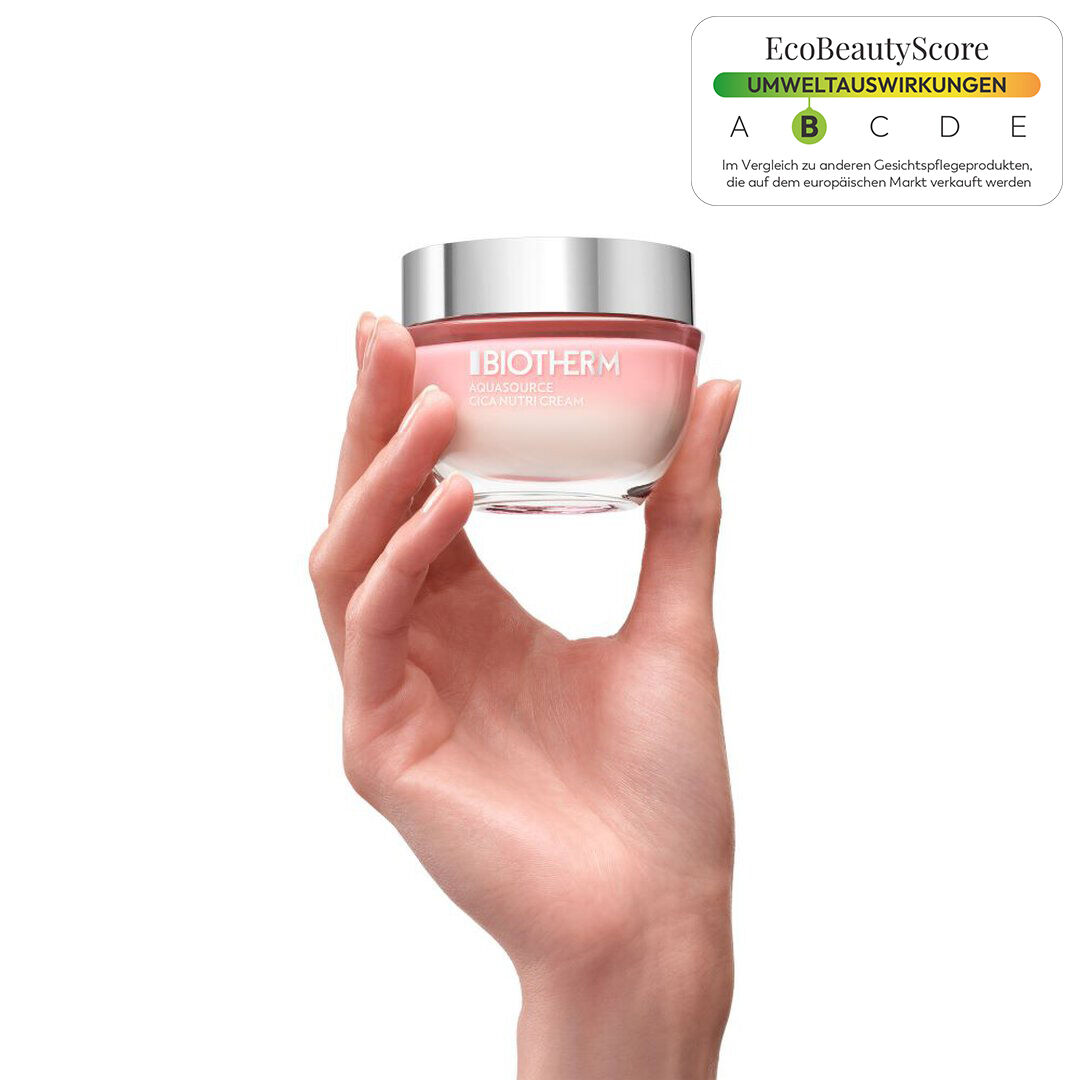 Eine Hand halt ein Glas mit rosa Creme, vor weißem Hintergrund.