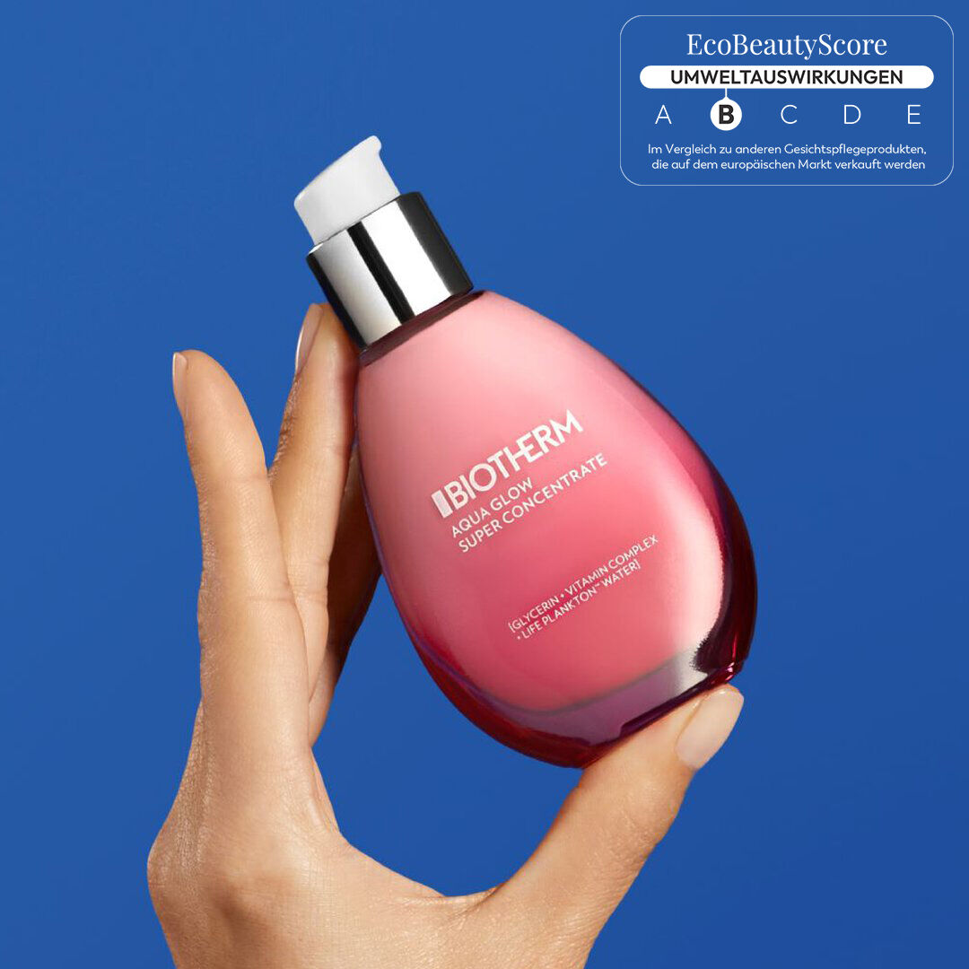 Eine Hand halt eine rosa Flasche Creme gegen einen blauen Hintergrund.