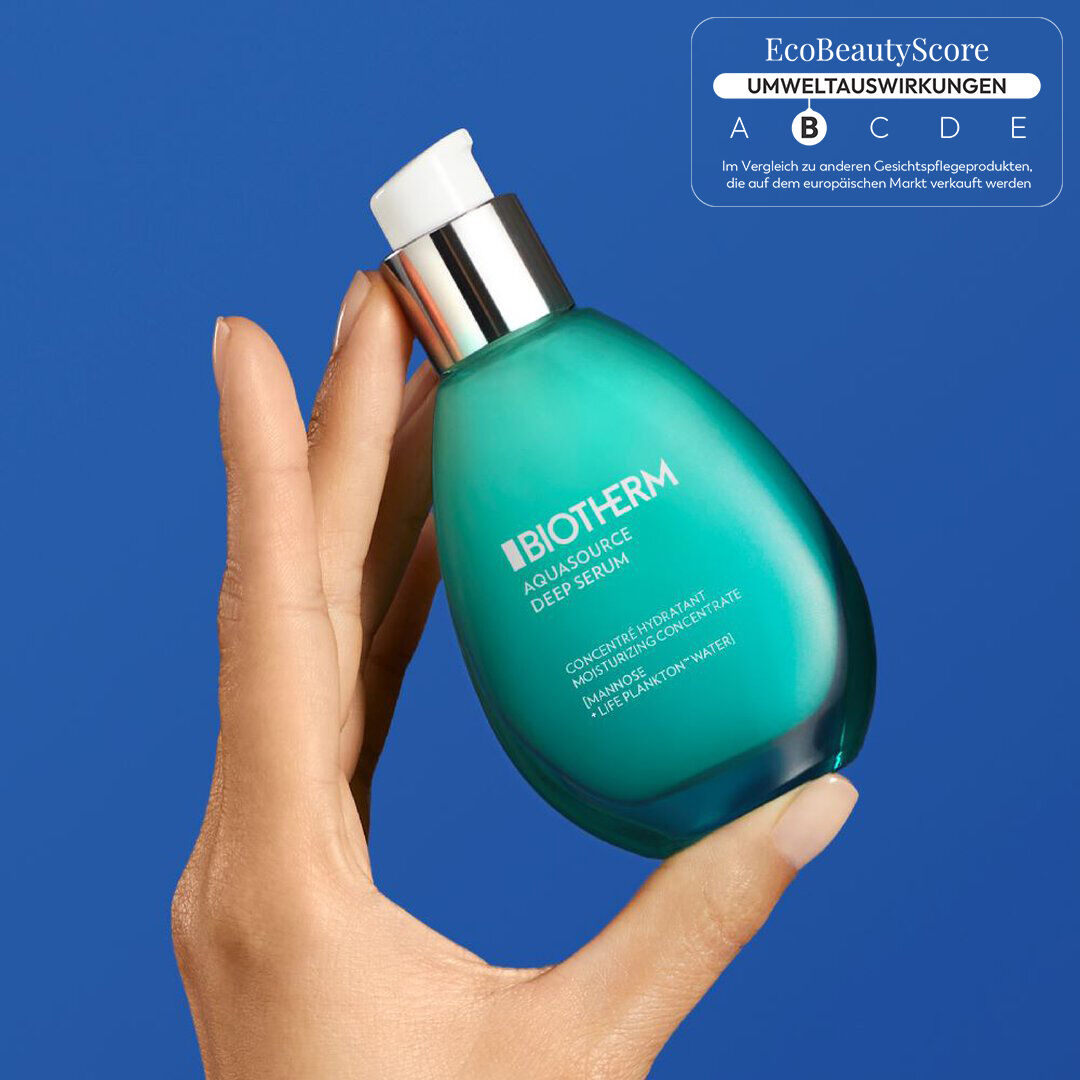 Hand halt eine grune Parfumflasche vor blauem Hintergrund.