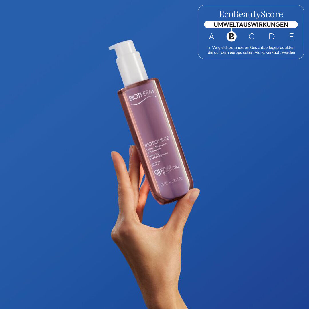 Hand halt eine rosa Spruhflasche vor blauem Hintergrund.