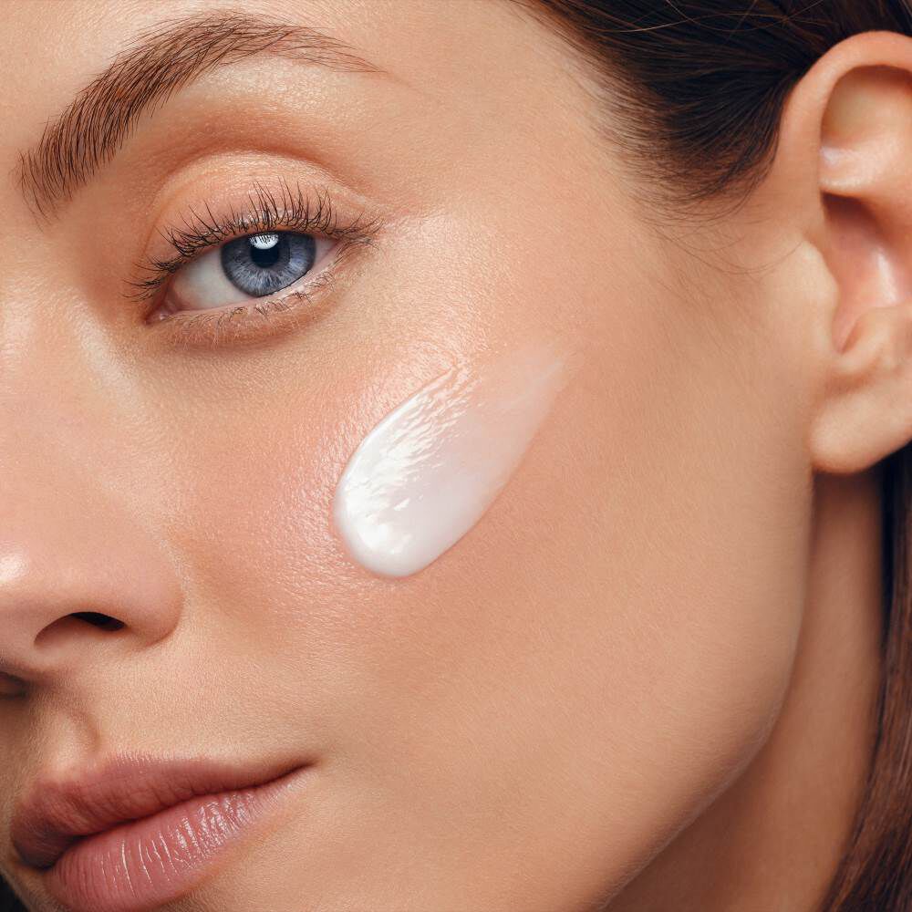 Gesicht mit Creme auf Wange, nahes Portrat, glatte Haut, neutraler Hintergrund.