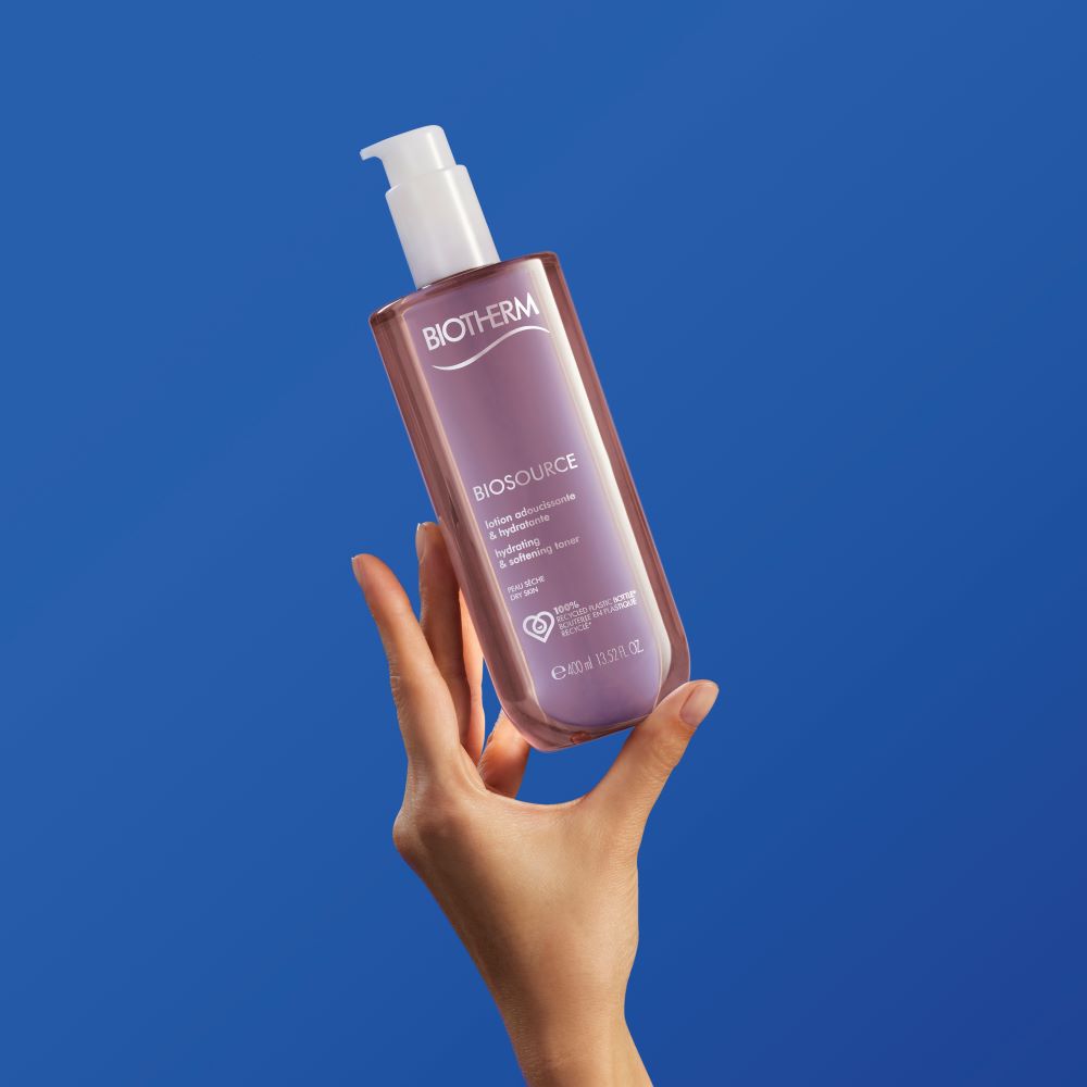 Eine Hand halt eine durchsichtige Flasche mit Pumpspender vor blauem Hintergrund.