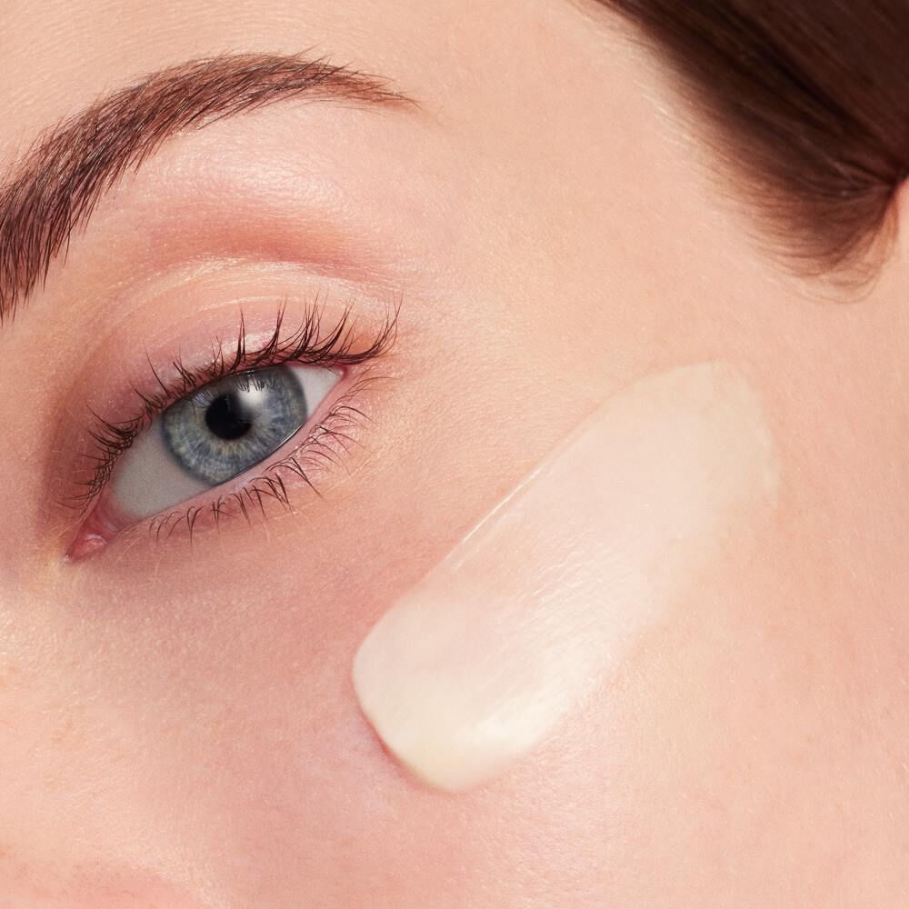 Creme wird auf eine Gesichtshaut aufgetragen, nahe dem Auge, in Nahaufnahme.