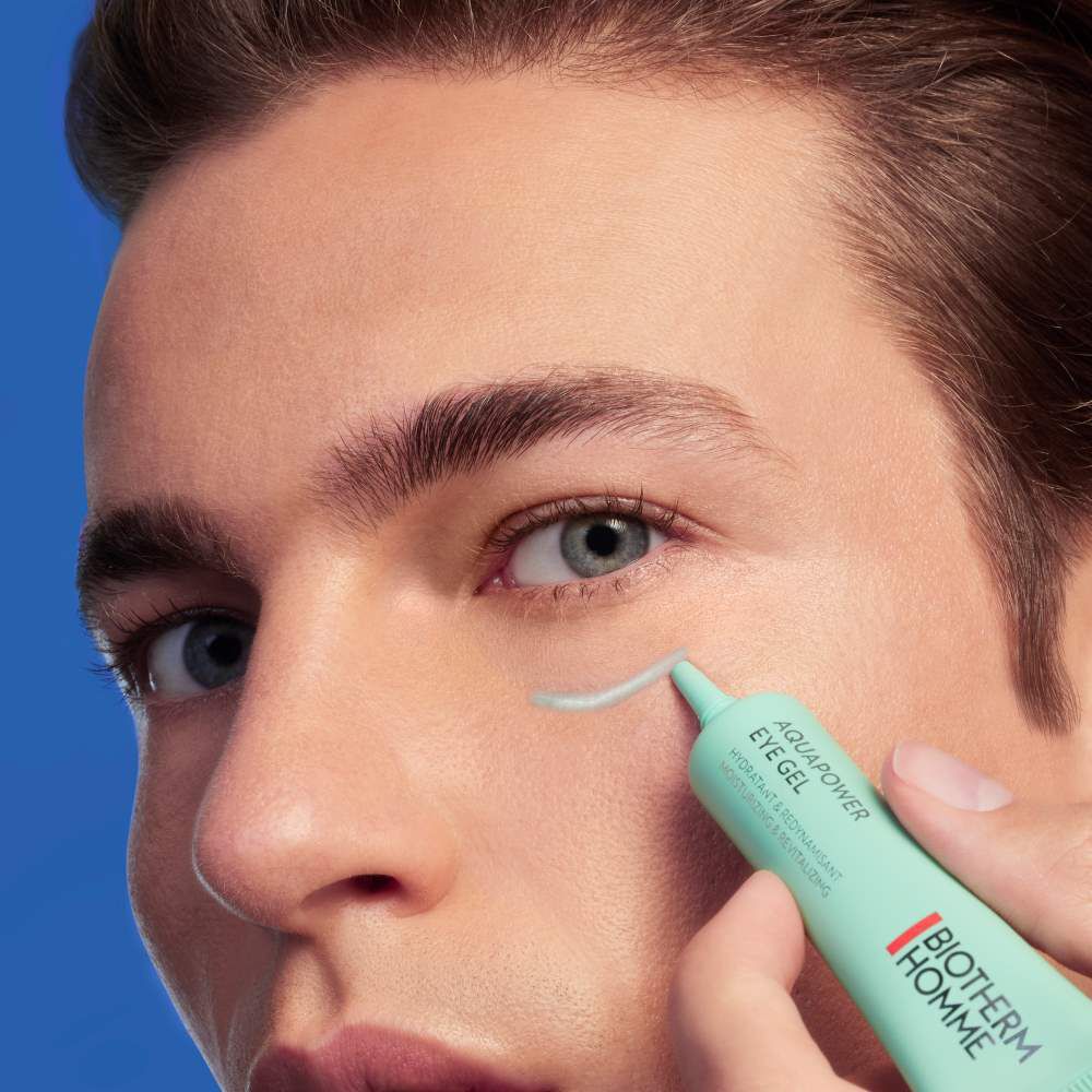 Person halt grunen Stift an Auge, blauer Hintergrund. Aktion erfolgt nahe am Gesicht.