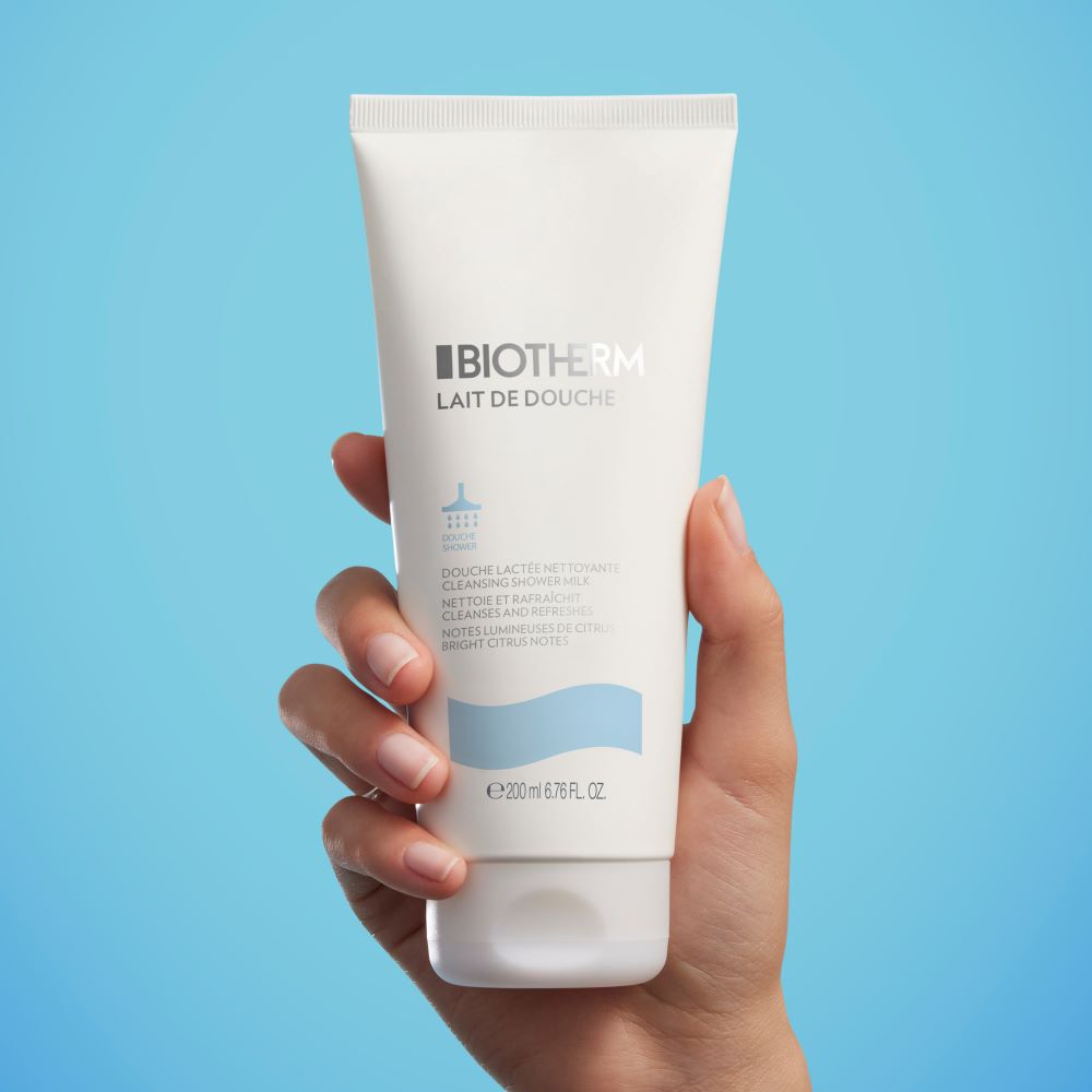 Hand halt weiße Kosmetiktube vor blauem Hintergrund; minimalistisch und modern prasentiert.