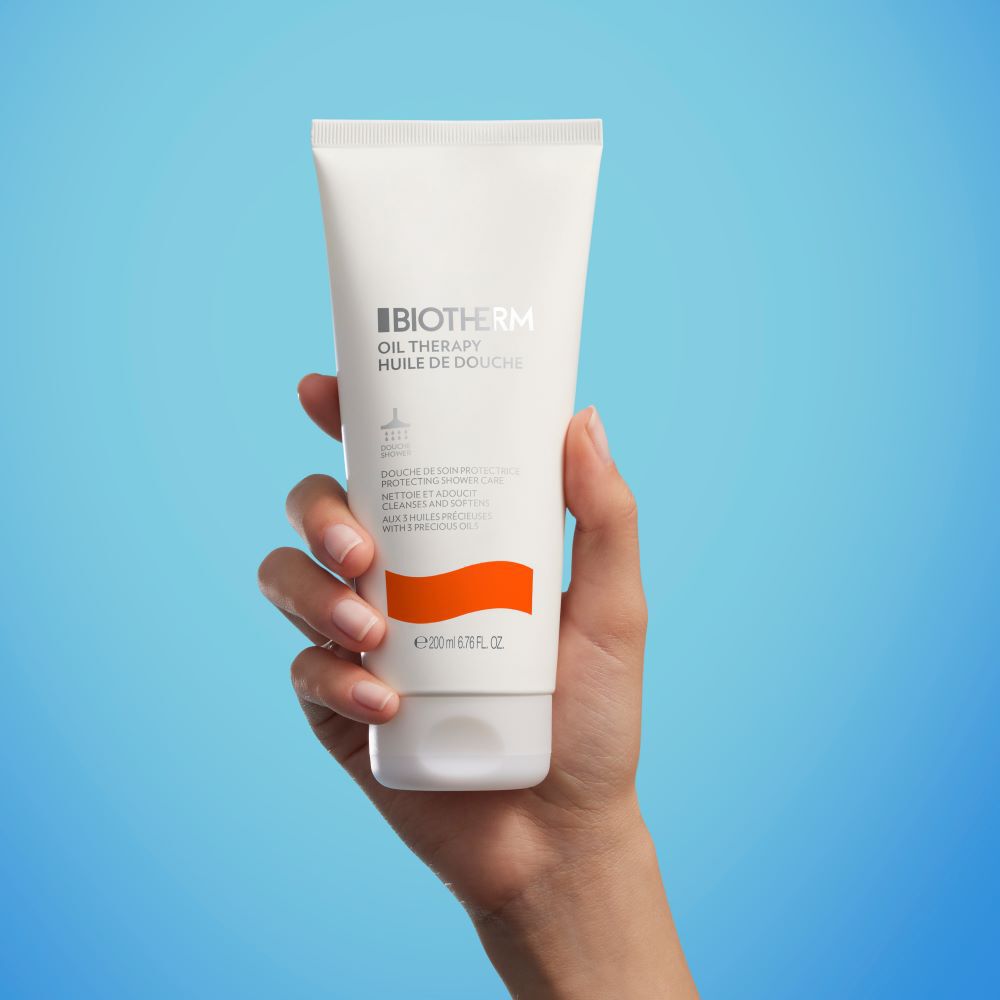 Hand halt eine weiße Tube vor blauem Hintergrund. Text auf Tube: „Moisturizing Cream“.