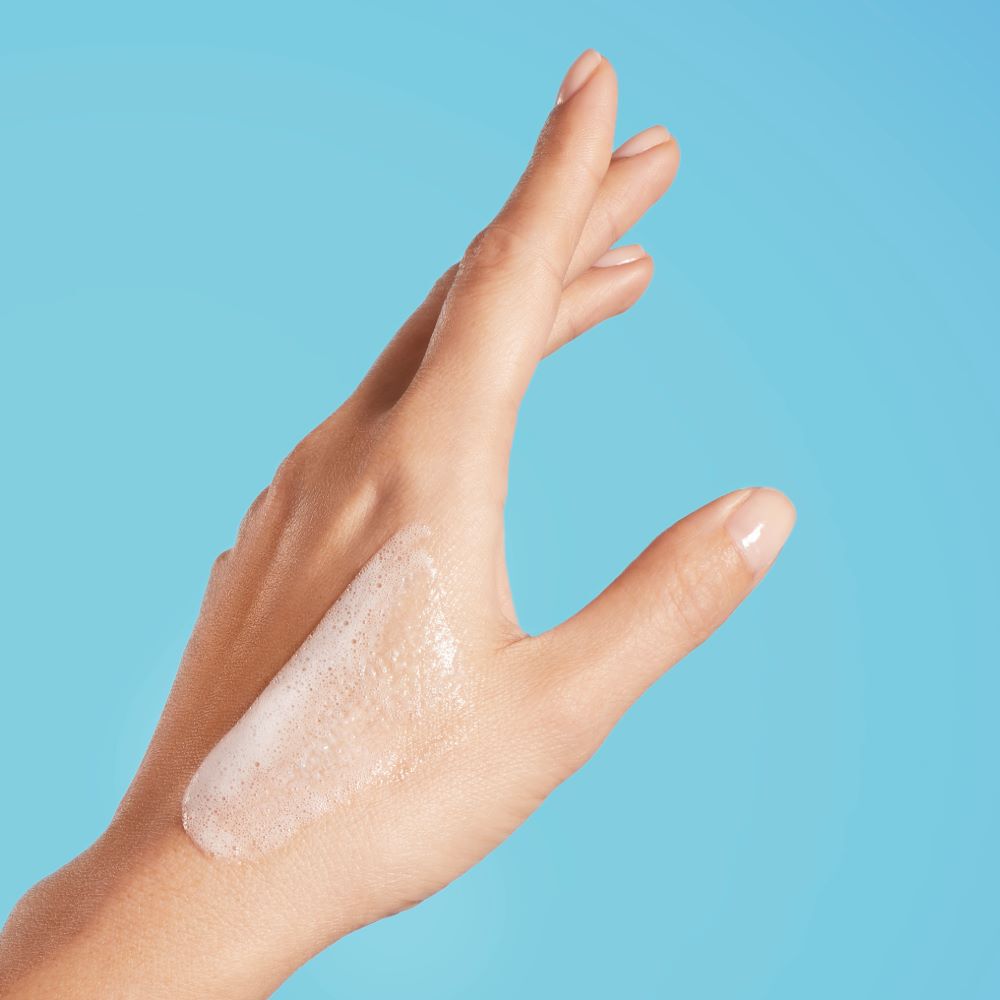 Hand mit Creme auf Haut vor blauem Hintergrund.