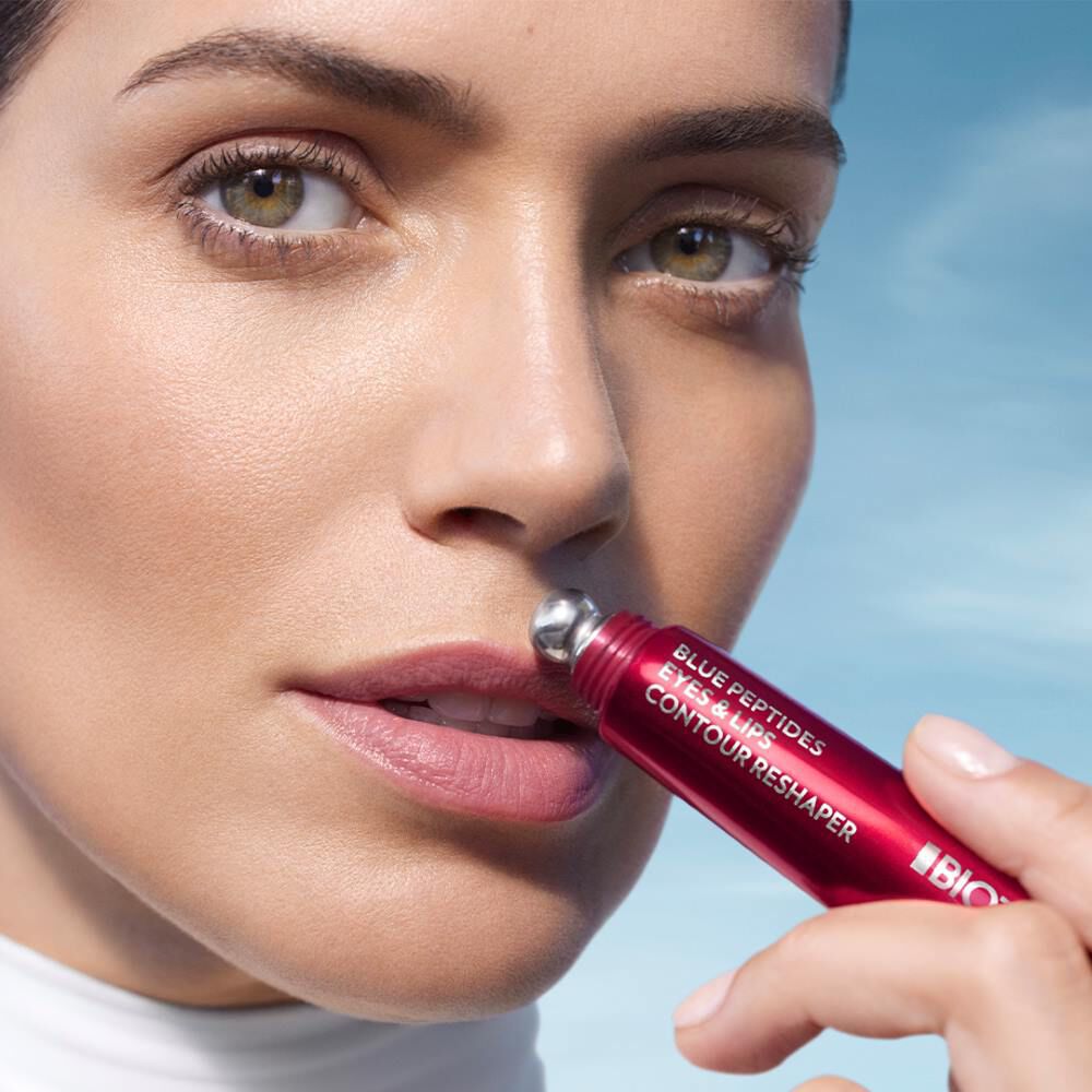 Eine Person halt einen roten Stift an den Mund, blauer Himmel im Hintergrund.