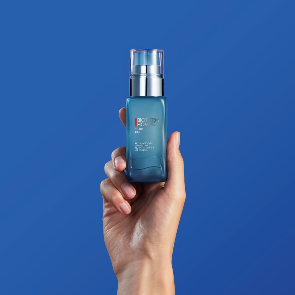 Hand halt eine blaue Parfumflasche vor blauem Hintergrund.