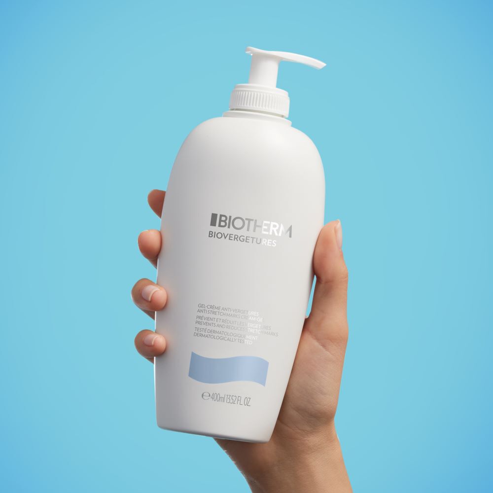 Hand halt eine weiße Flasche mit Pumpspender vor blauem Hintergrund.