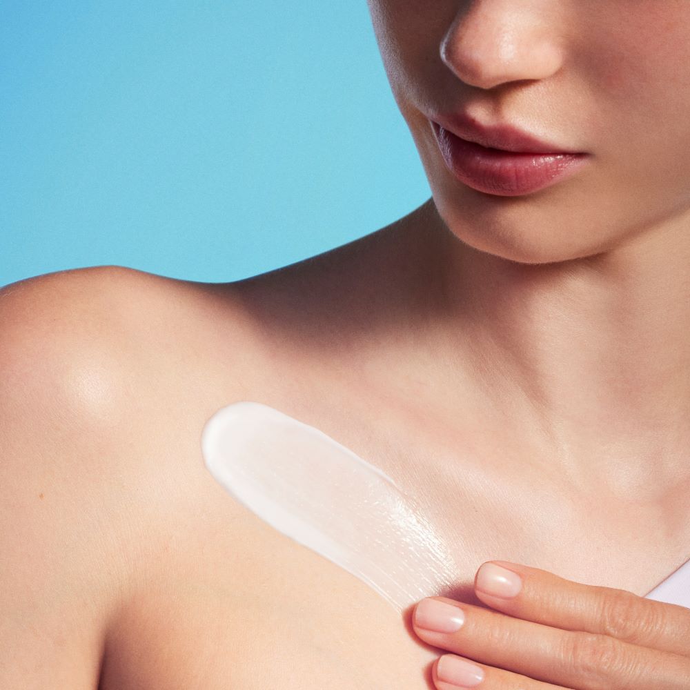 Eine Person legt ein transparentes Pflaster auf die Schulter. Hintergrund in hellem Blau.