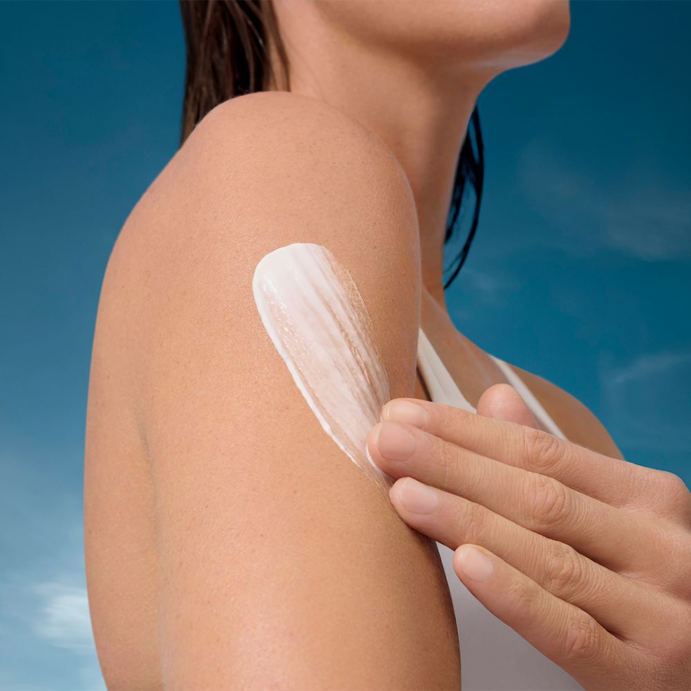 Lotion wird auf einen Arm aufgetragen; Hintergrund ist ein blauer Himmel.