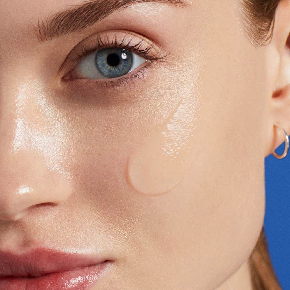 Nahaufnahme eines Gesichts mit Tropfen auf der Haut vor blauem Hintergrund.