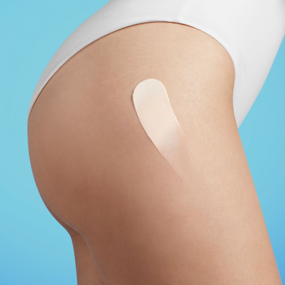 Haut mit Lotion, aufgetragen auf Oberschenkel, vor blauem Hintergrund.
