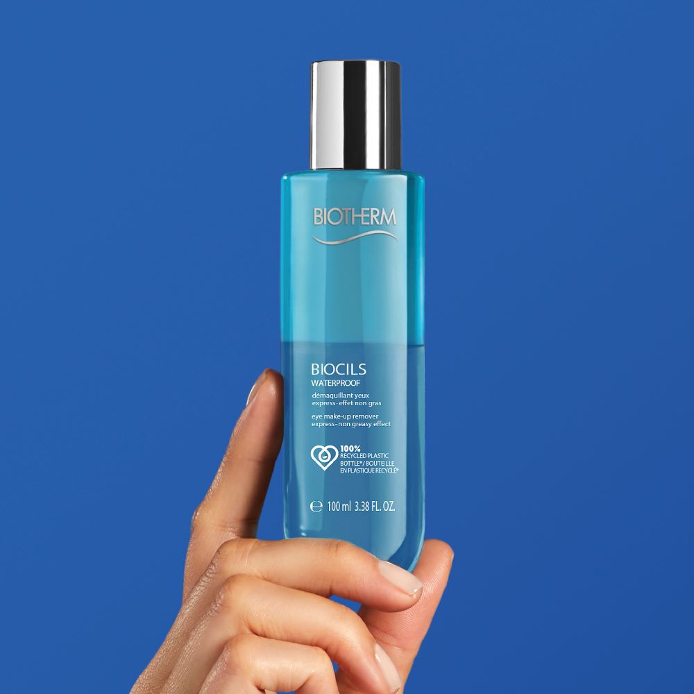 Hand halt blaue Flasche mit silbernem Verschluss vor blauem Hintergrund.