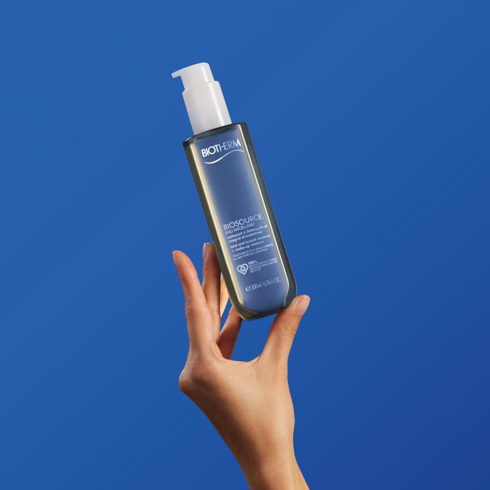 Hand halt eine durchsichtige Flasche mit Pumpspender vor blauem Hintergrund hoch.