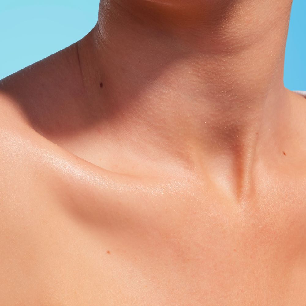 Hals und Schlusselbein, sonnenbeleuchtet, vor einem blauen Hintergrund.