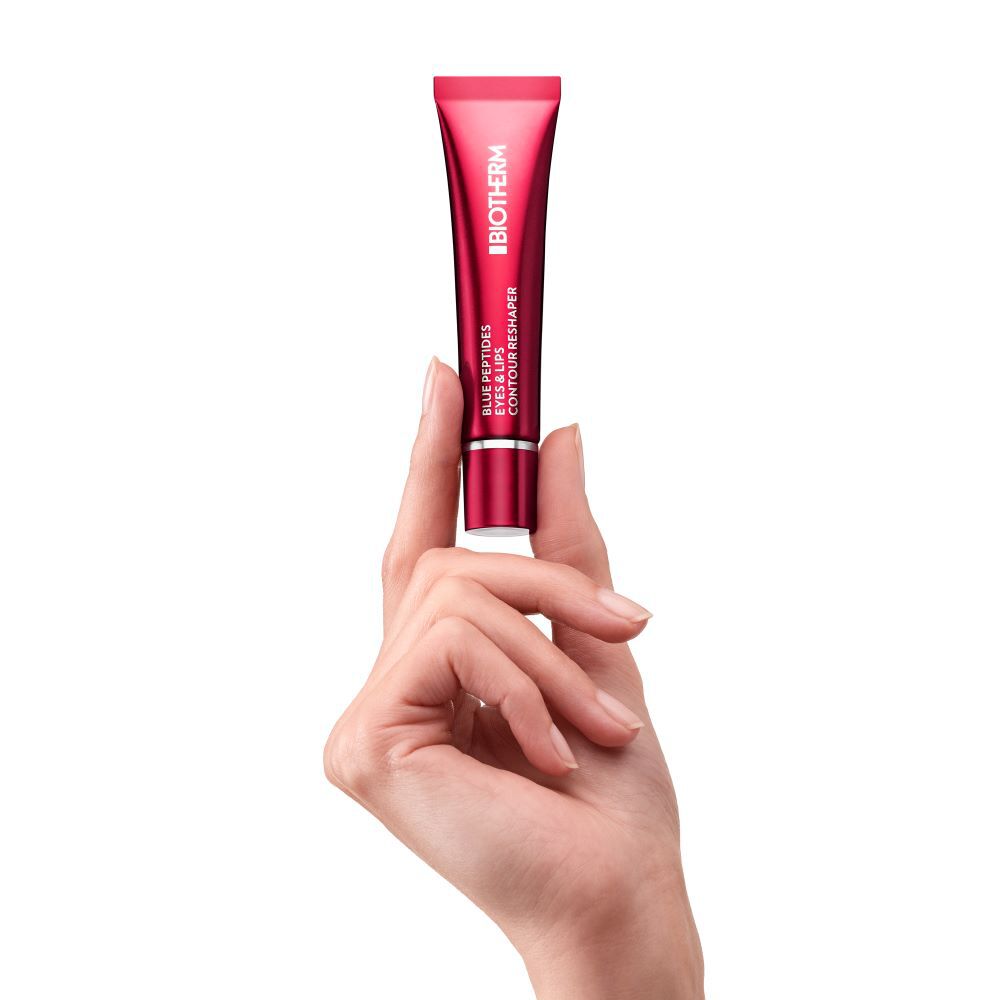 Eine Hand halt eine rote, stehende Creme-Tube auf einem weißen Hintergrund.