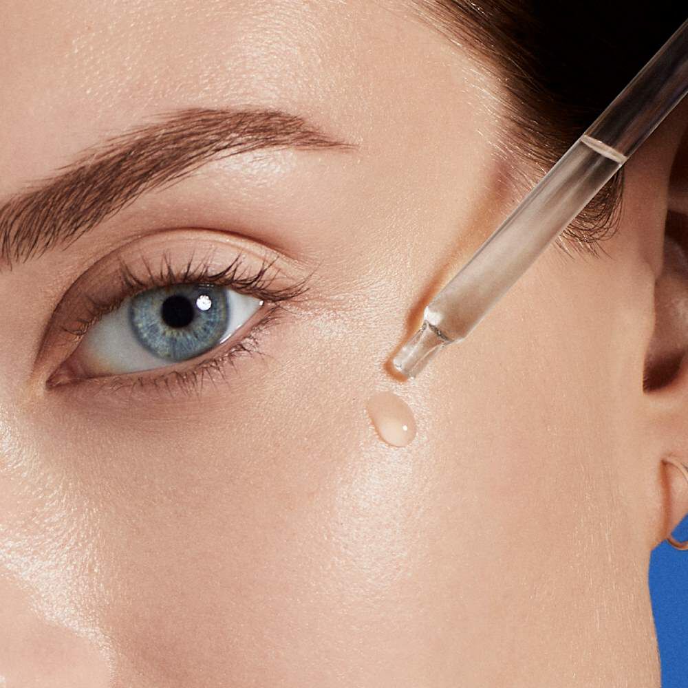 Pipette gibt Serum unter Auge auf Haut, Nahaufnahme, blauer Hintergrund.